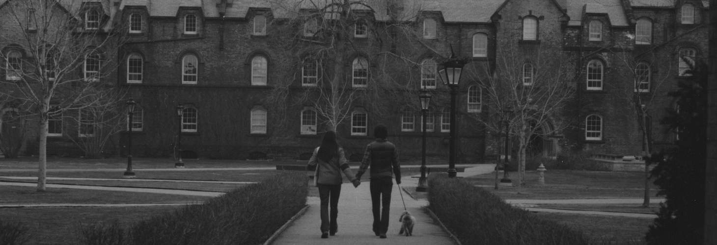 Two people walking with a dog, seen through an archway, with University College in background