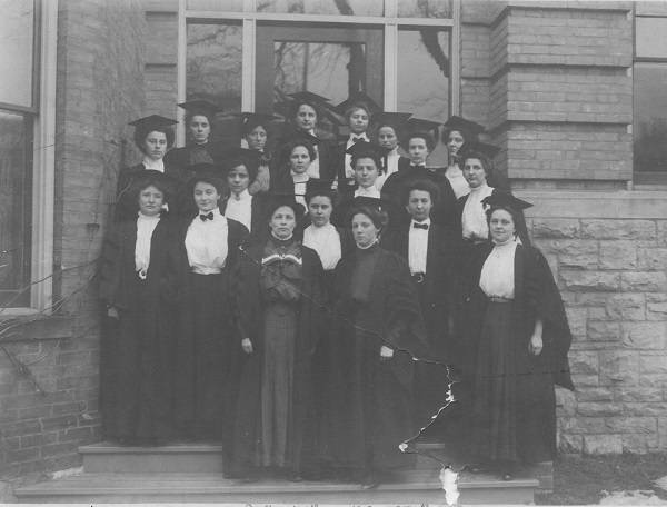 About 20 women posing in doorway of building, wearing academic robes and mortarboards