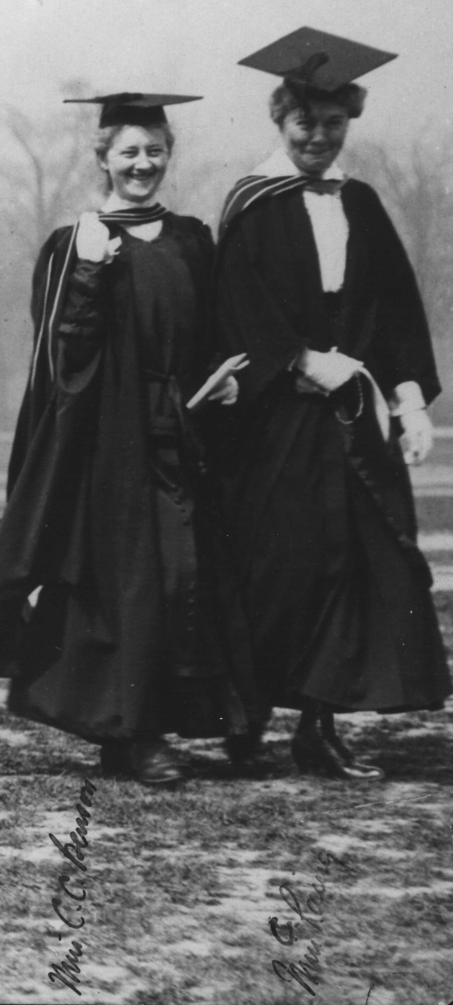 two women in academic robes and mortarbards, walking and smiling