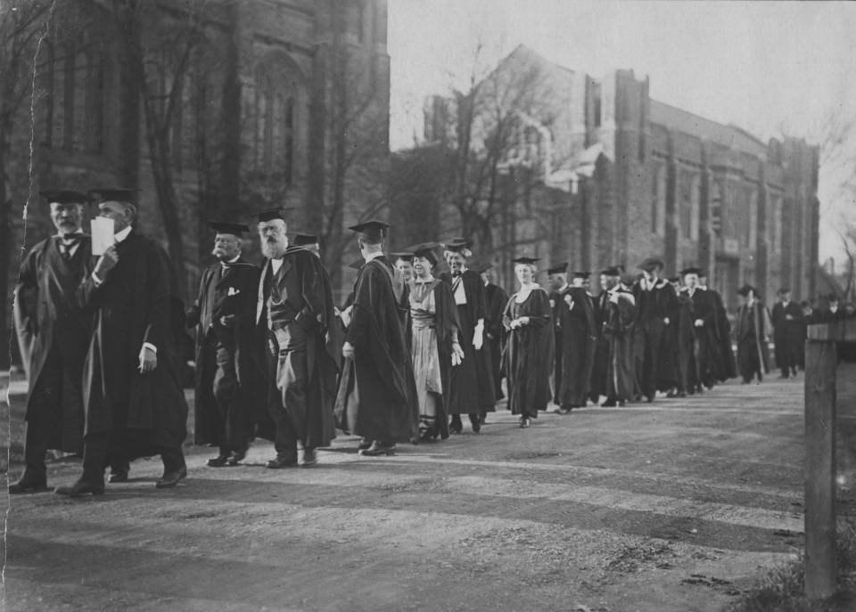 Over twenty people in academic robes walking in a procession