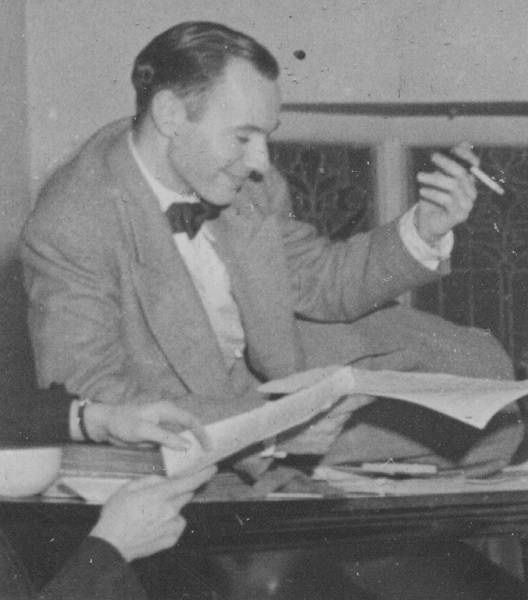 Man in suit with a cigarette in one hand and paper in the other, smiling