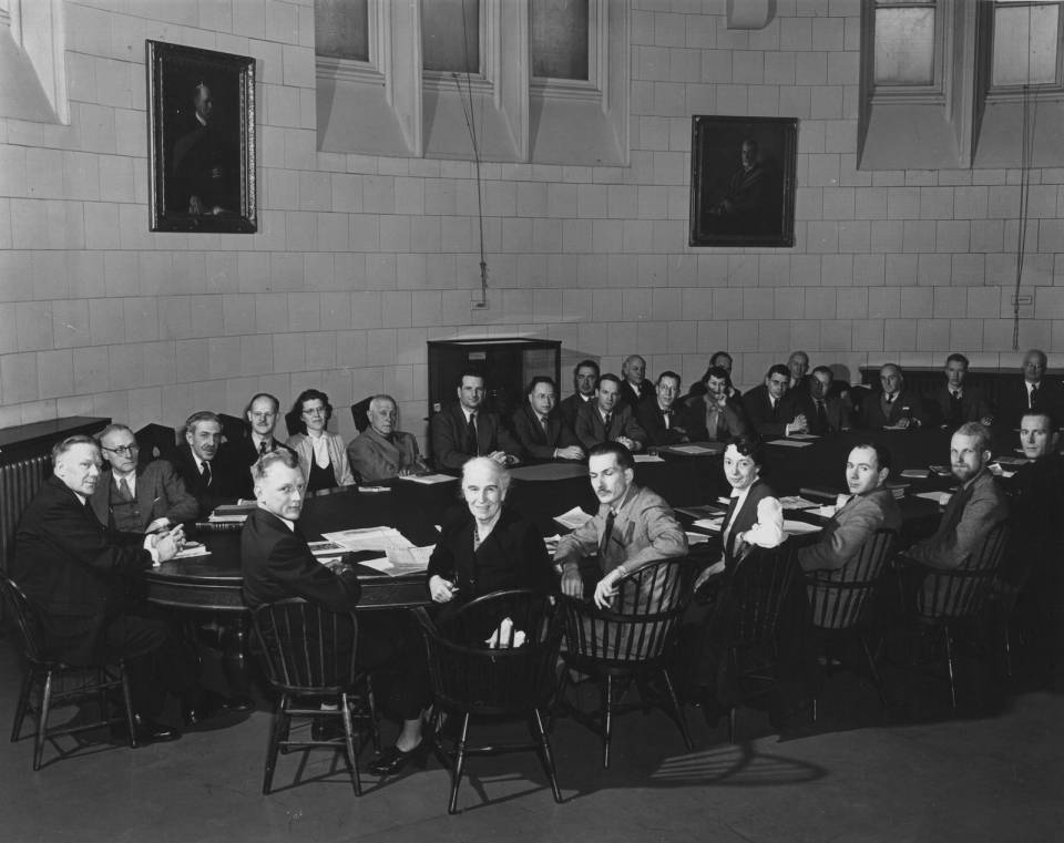 About thirty people sitting around a large oval table, including about four women