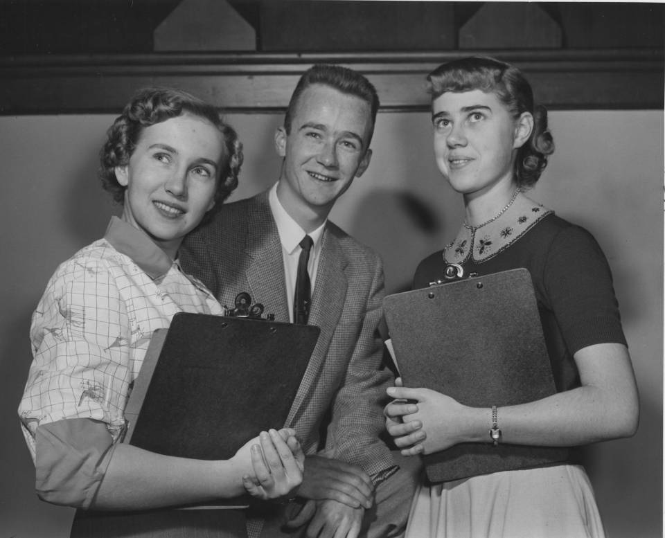 A young man and two young women holding clipboards