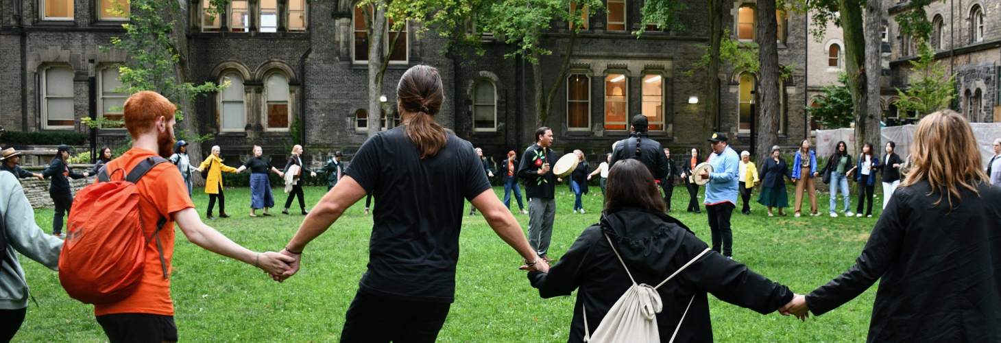 people holding hands in a round dance in the UC quad