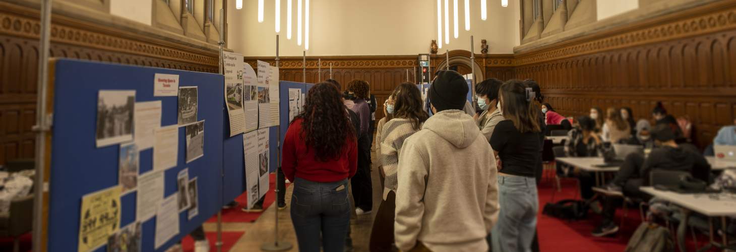 Students gathered around poster boards in a large, gothic hall