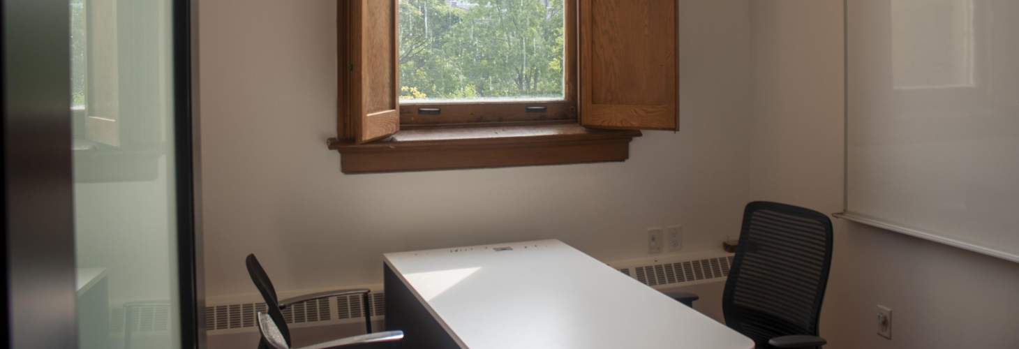 A small meeting room with two chairs, table, and shutter windows