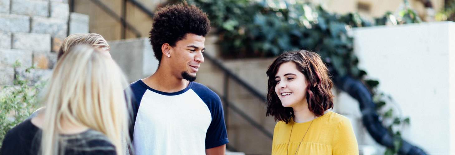 Three students casually talking outside campus building in summer