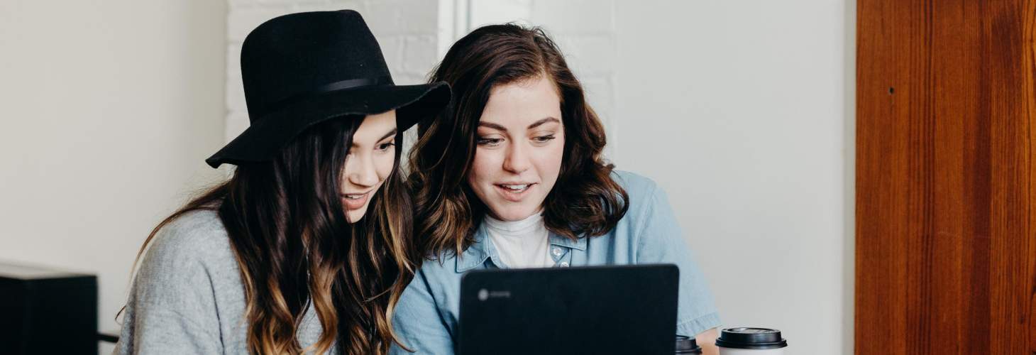 Two female students sitting at a table looking at a laptop