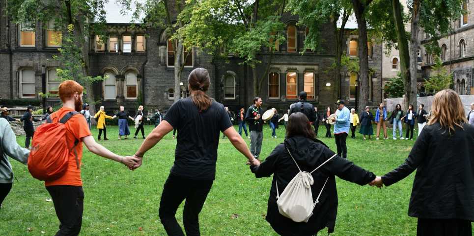 people holding hands in a round dance in the UC quad