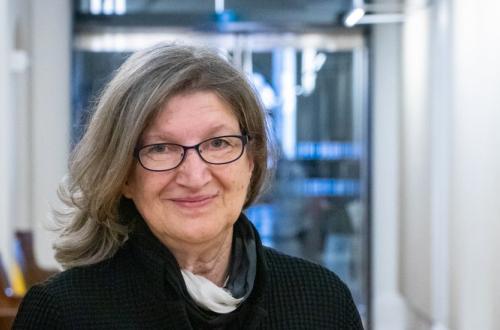 Barbara Fischer wearing black-rimmed glasses, standing in front of a glass doorway