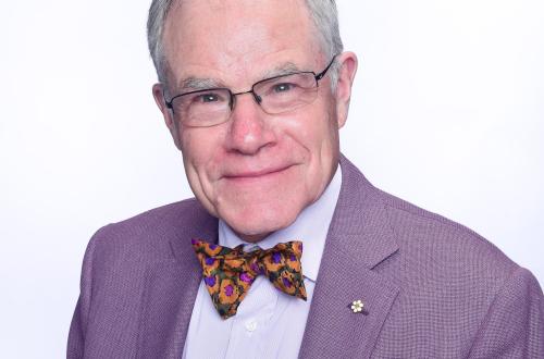 Portrait of an older white man with grey hair, glasses, and bow-tie