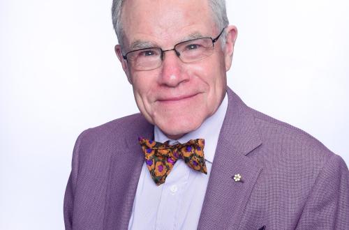 Portrait of a man with white hair, glasses and bowtie