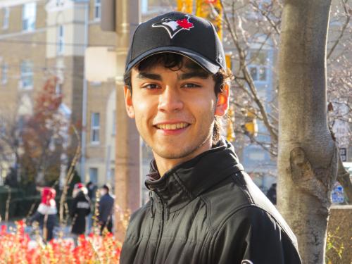 An image of Max-Ray Ellis. The student is wearing a blue jay's baseball cap and is standing in front of a tree. 