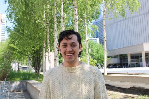 Student Cameron Miranda-Radbord is smiling in front of trees and is wearing a beige wool sweater. 