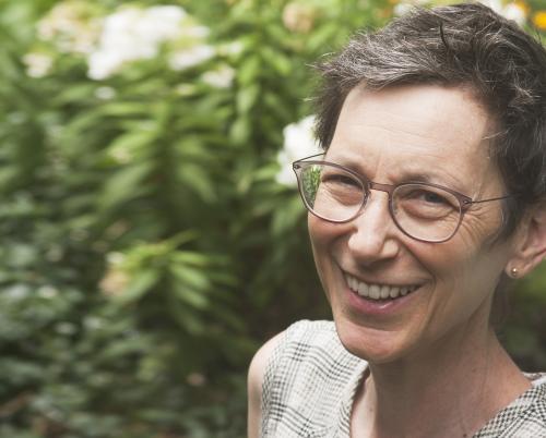 Jane Wolff wearing glasses and smiling in front of greenery and flowers