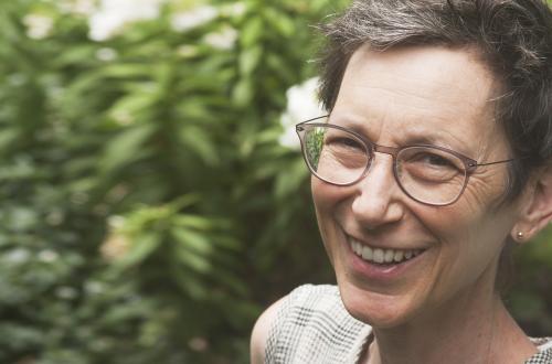 Jane Wolff wearing glasses and smiling in front of greenery and flowers