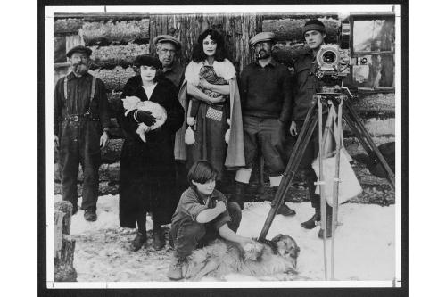 Archival black and white photo of a family posing with camera beside log cabin