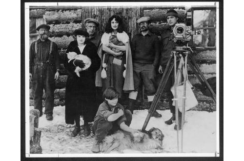 Archival black and white photo of a family posing with camera beside log cabin