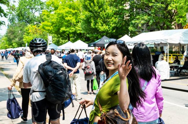 A woman looks back at the camera and waves as she and others walk down St. George St., which is lined with tents and activities for all ages