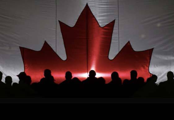Silhouette of people in front of stage with huge Canadian flag