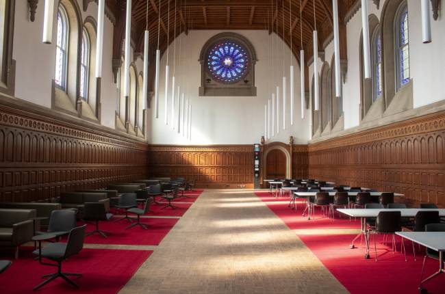 Large hall with red carpets, lounge furniture, and stained-glass window