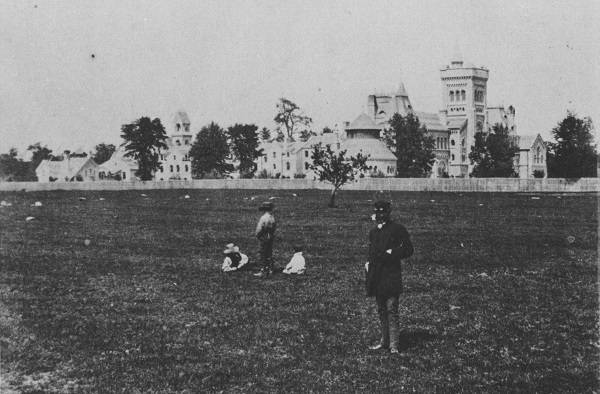 Field in foreground with man and children, University College in background