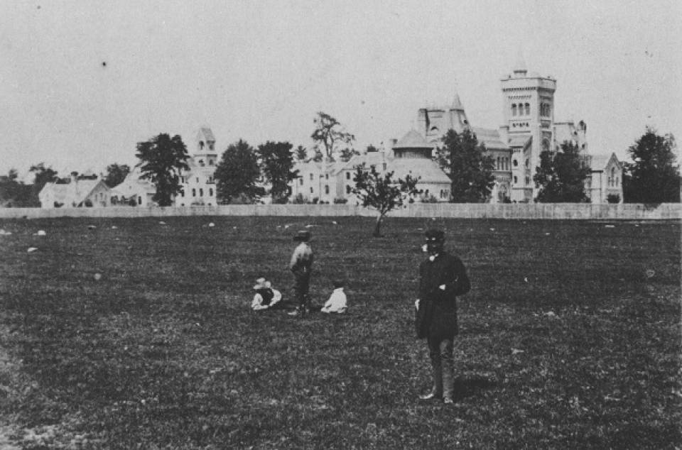 Field in foreground with man and children, University College in background