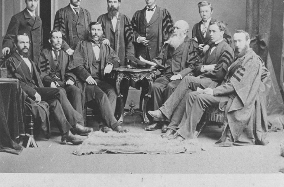 Group of 11 men, most wearing academic robes