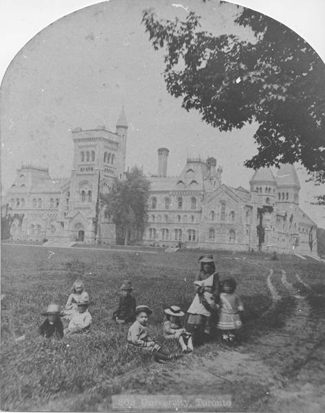 Eight children on grass with University College in background