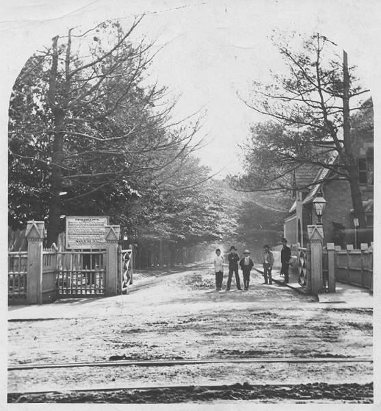 Gates with men and boys standing in entrance, with tree-lined street behind