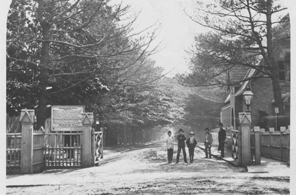 Gates with men and boys standing in entrance, with tree-lined street behind