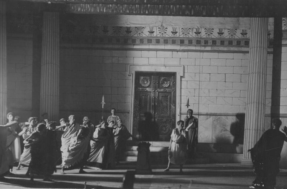 About a dozen actors performing on stage in classical costume