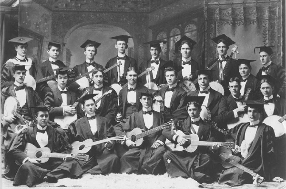 About 20 men, each holding a banjo or guitar, dressed in academic robes and mortarboards