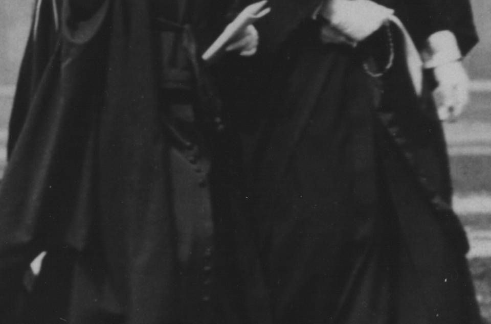 two women in academic robes and mortarbards, walking and smiling