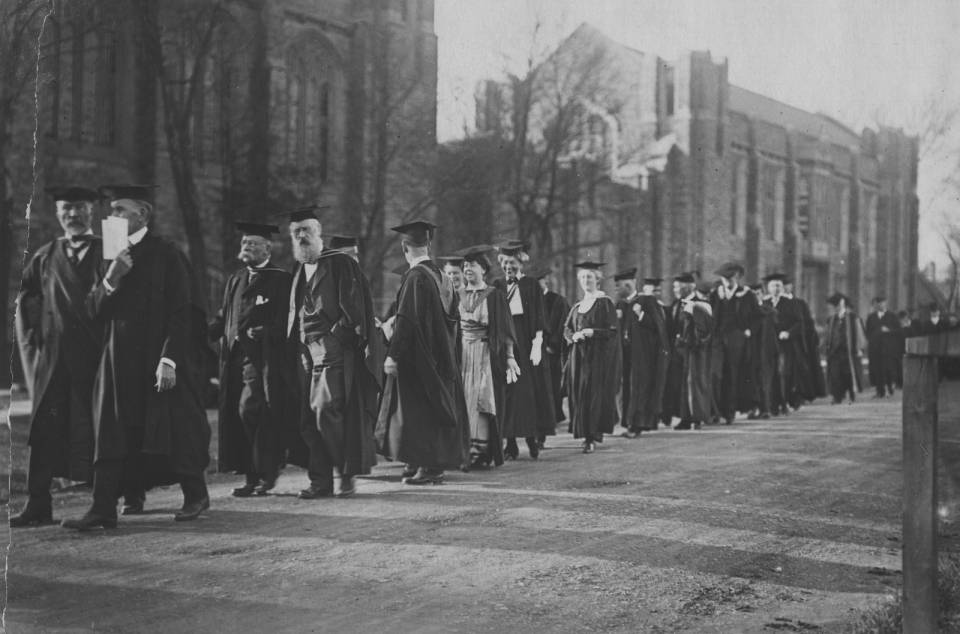 Over twenty people in academic robes walking in a procession