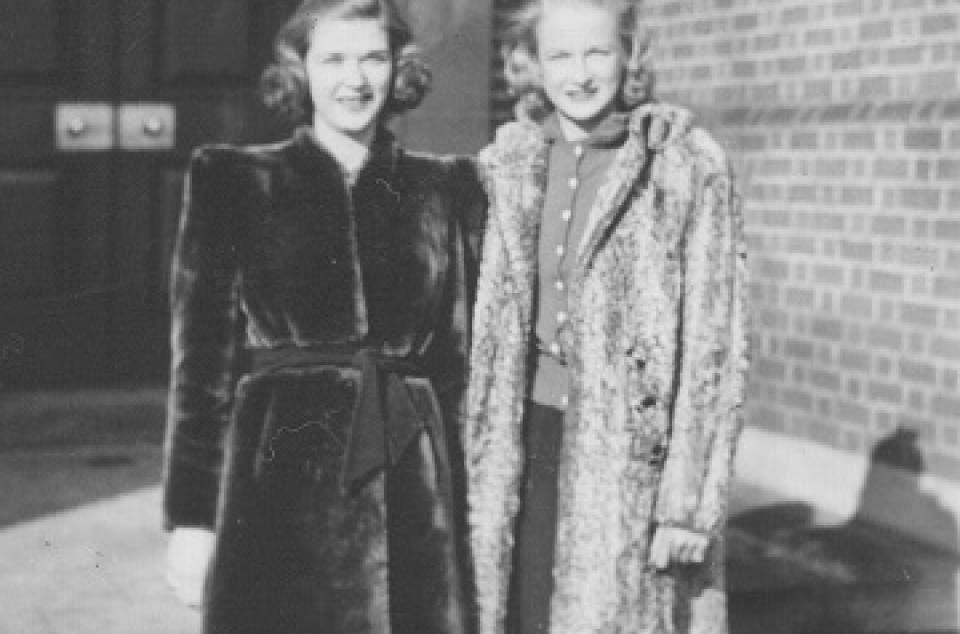 two young women in coats, with Whitney Hall behind them