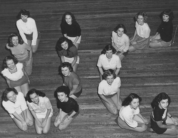 Sixteen young women kneeling on floor to form the letters "UC"