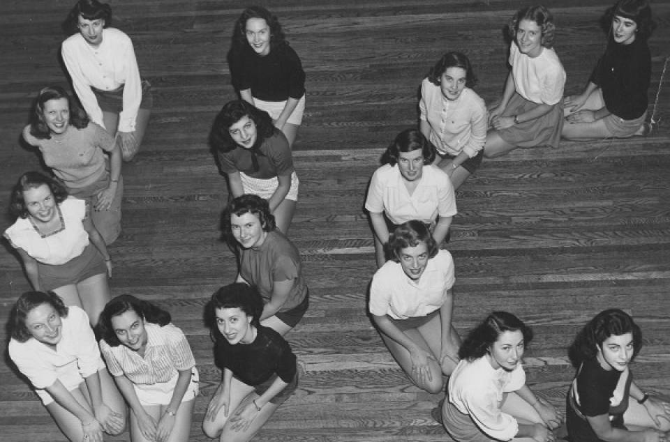 Sixteen young women kneeling on floor to form the letters "UC"