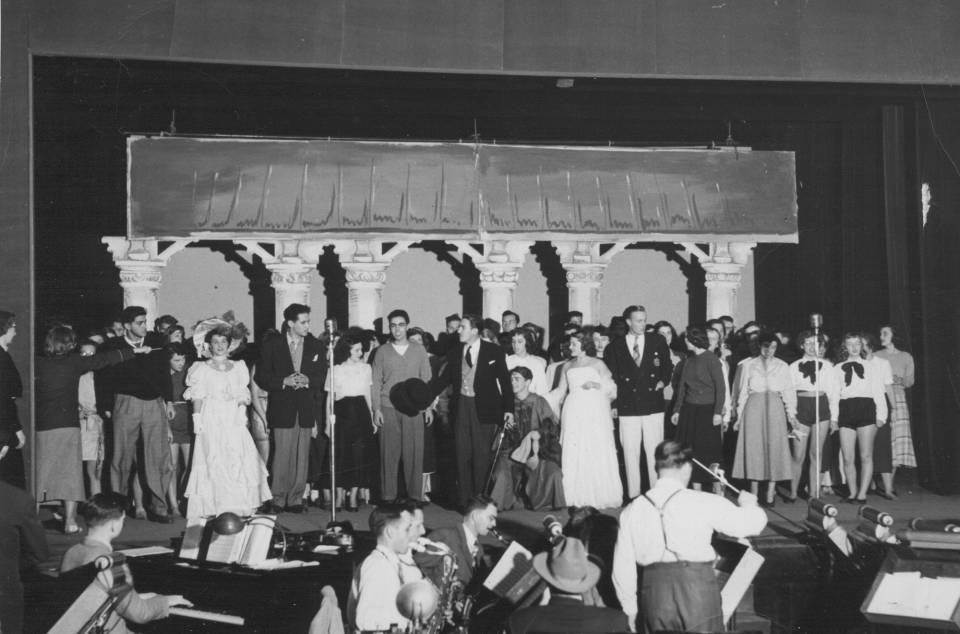 dozens of performers on stage, with musicians and conductor in the foreground