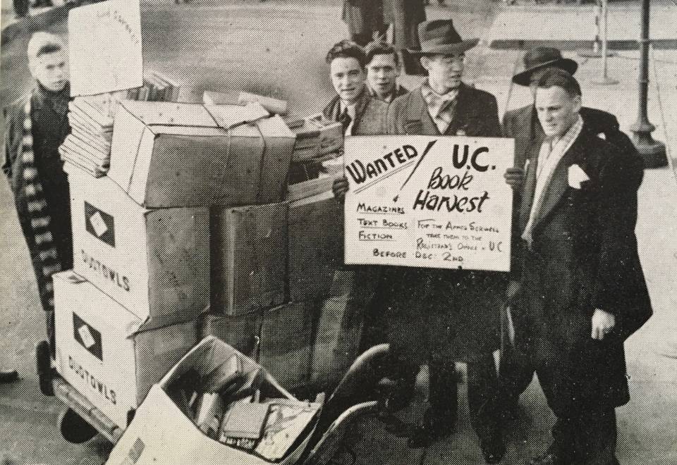 Six men with boxes of books and magazines, with a sign that says "U.C. Book Harvest for the Armed Services"