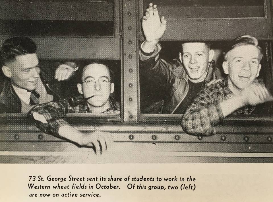 four young men looking out the window of a train, smiling and waving