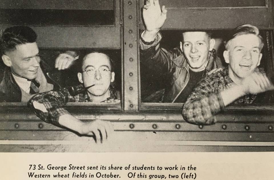 four young men looking out the window of a train, smiling and waving