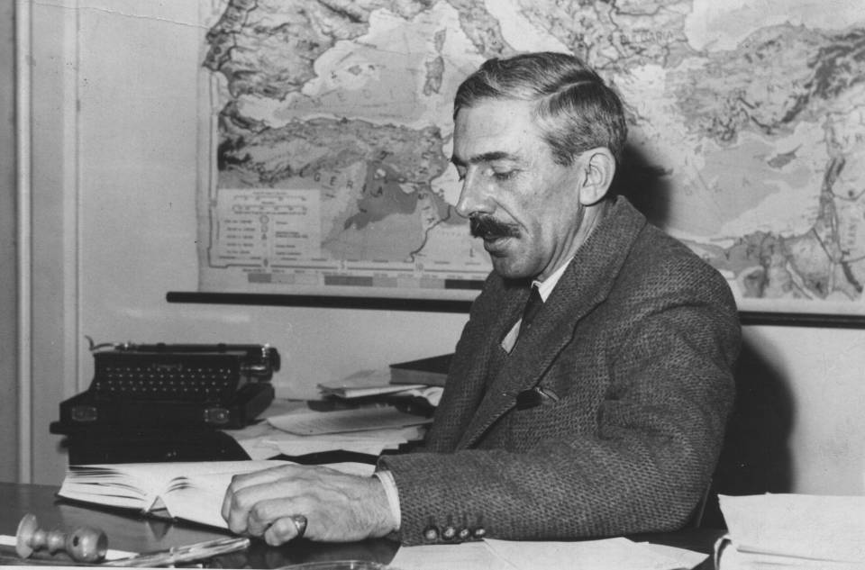professor sitting at desk, with map and typewriter in background