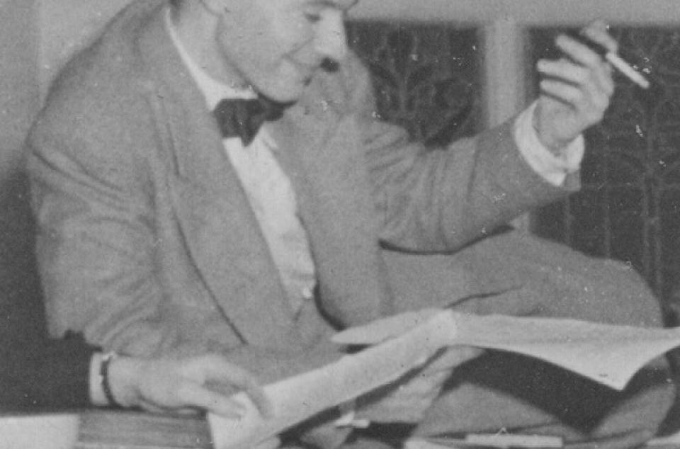 Man in suit with a cigarette in one hand and paper in the other, smiling