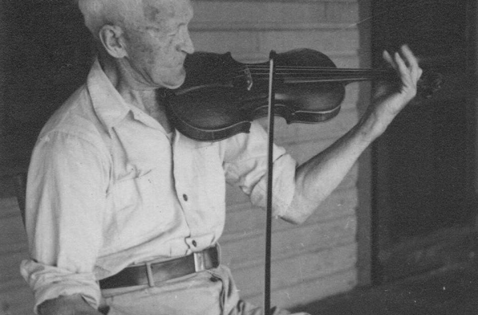 Elderly man sitting on a porch, playing a violin