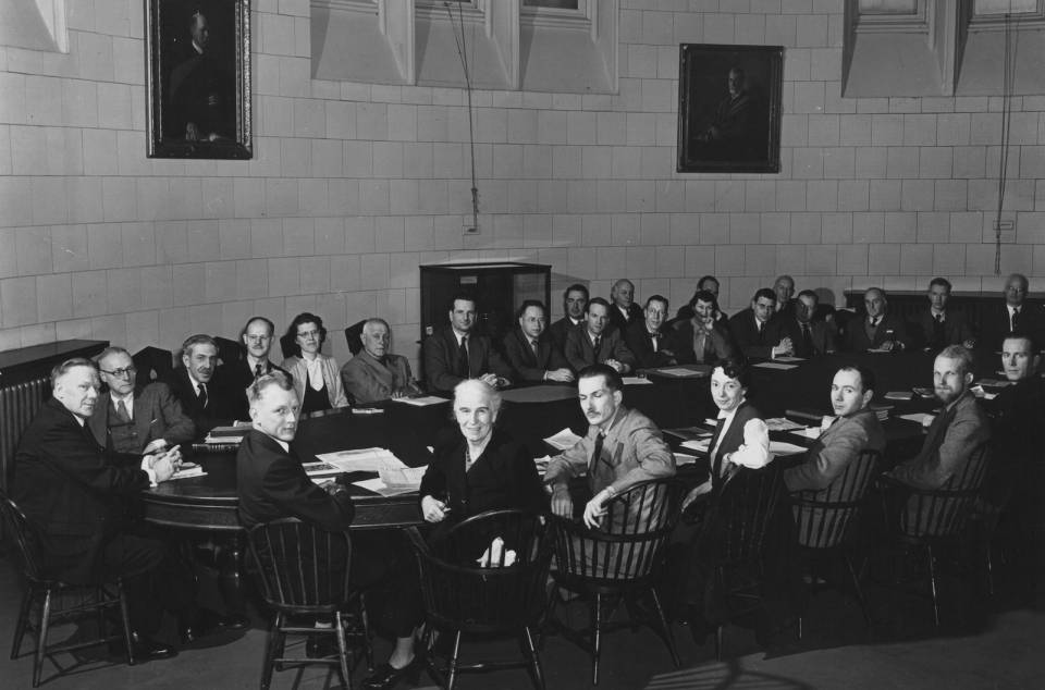 About thirty people sitting around a large oval table, including about four women