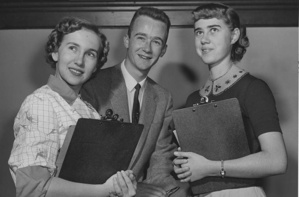 A young man and two young women holding clipboards