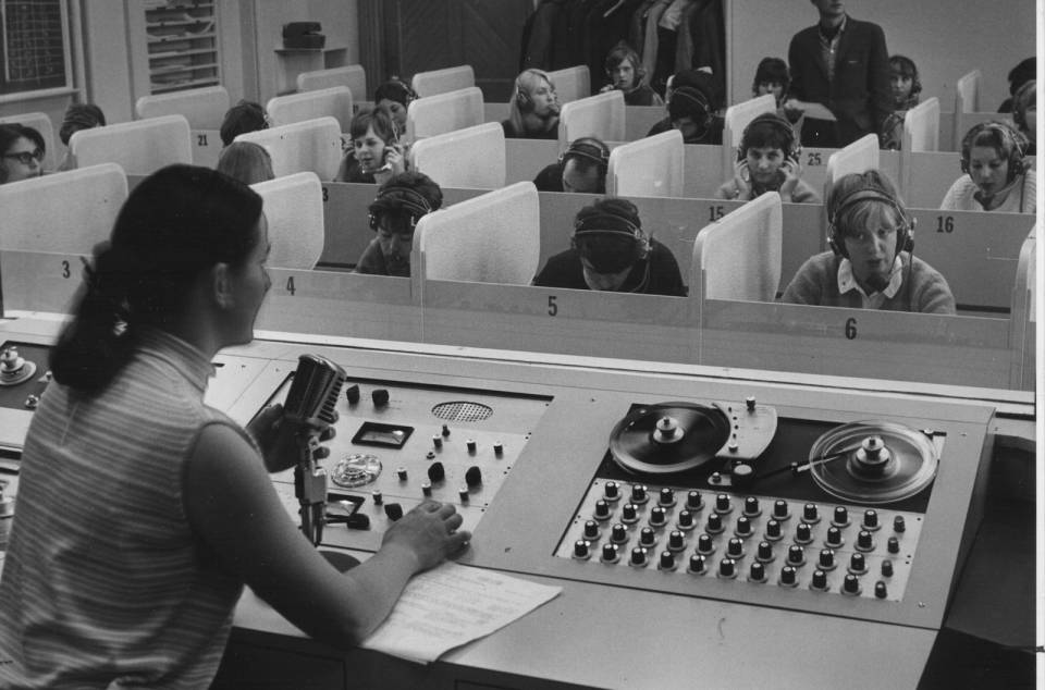 Two teachers and about fifteen students (with headphones) in a language lab