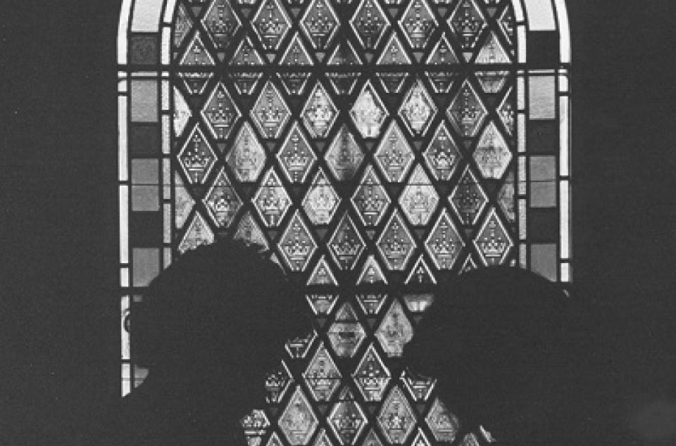 Silhouettes of two people seemingly holding books, in front of stained glass window