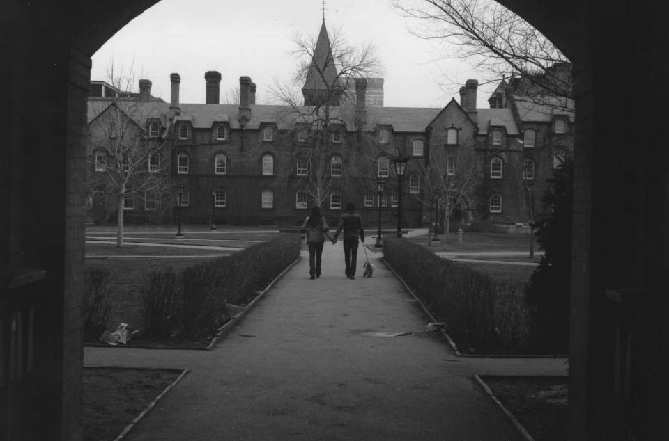 Two people walking with a dog, seen through an archway, with University College in background